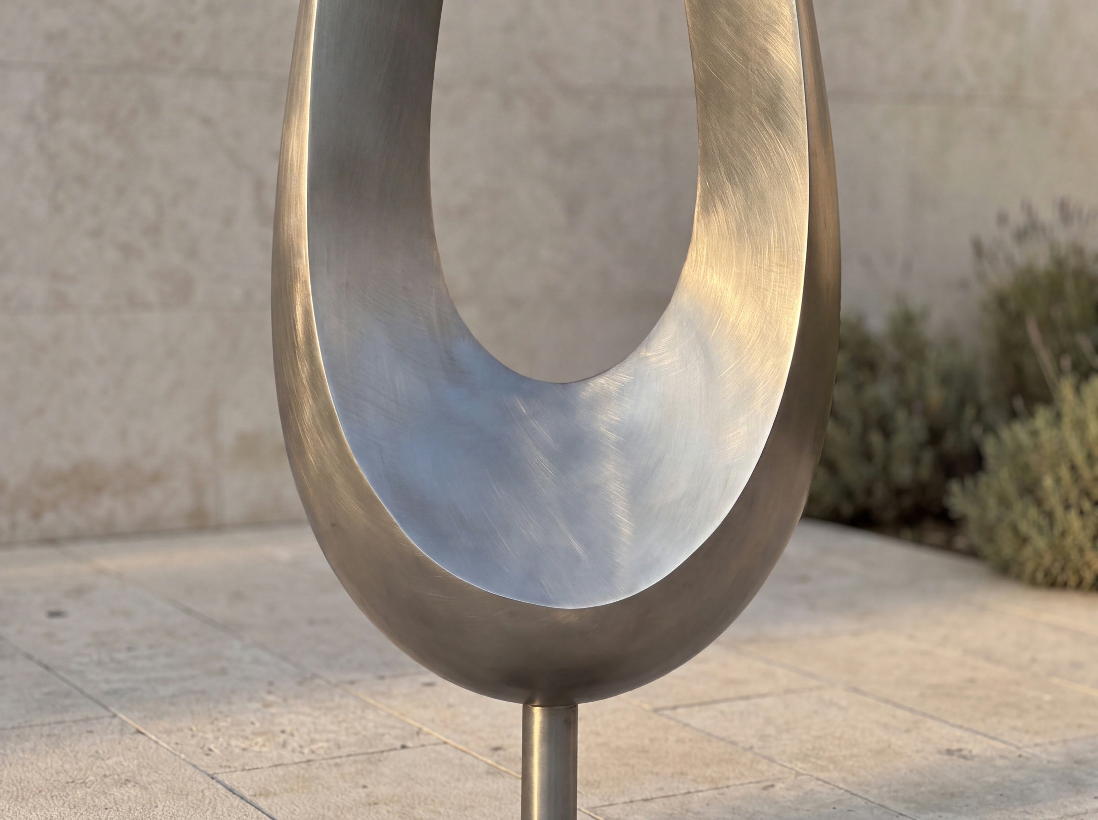 Close view of the brushed steel surface and curved lower body of the open-form sculpture