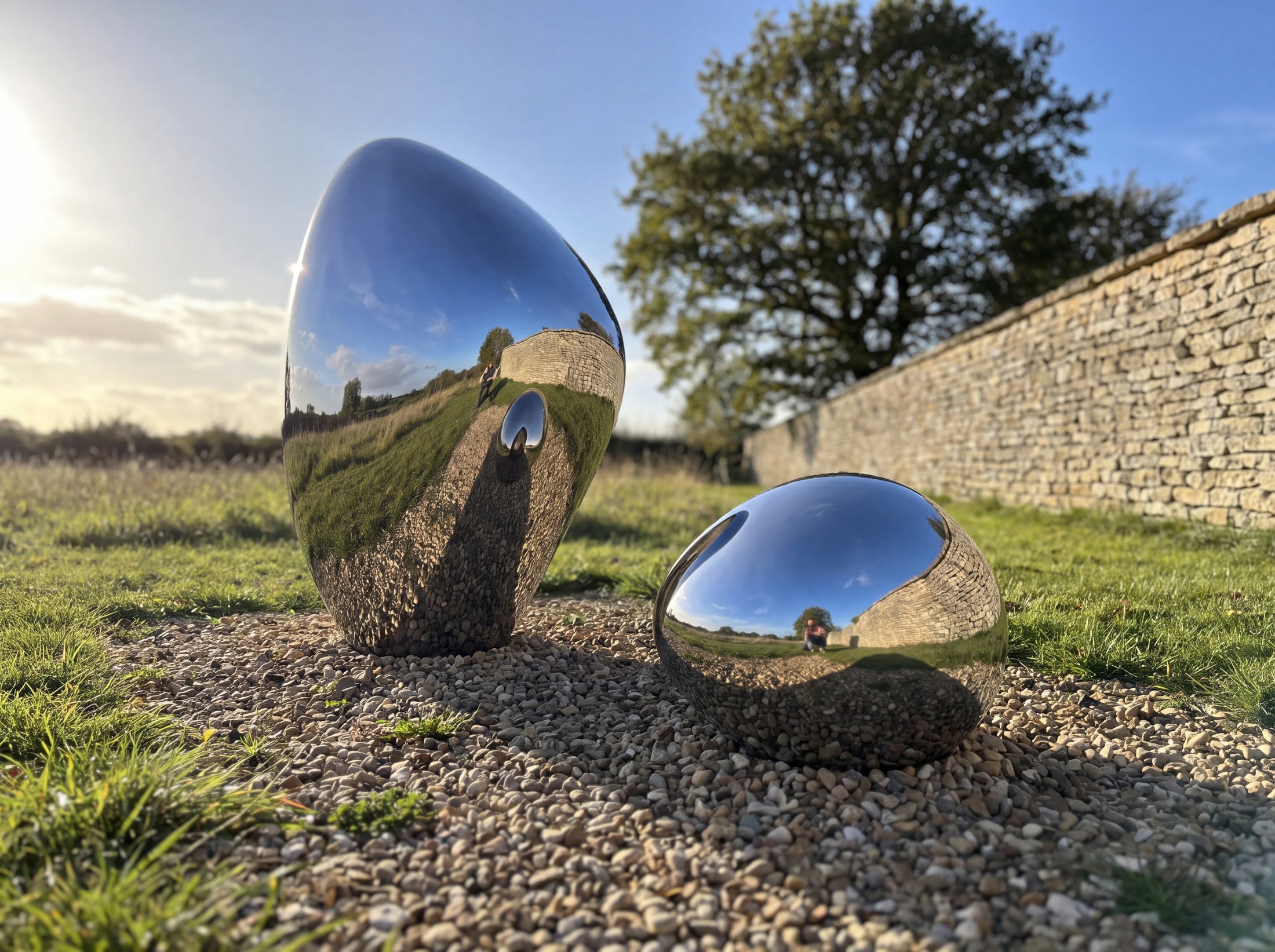 Low-angle view of one upright and one low mirror-polished steel stone in a garden