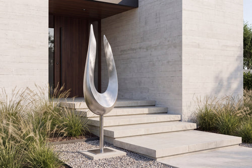 Brushed stainless steel open-form sculpture beside a landscaped entrance
