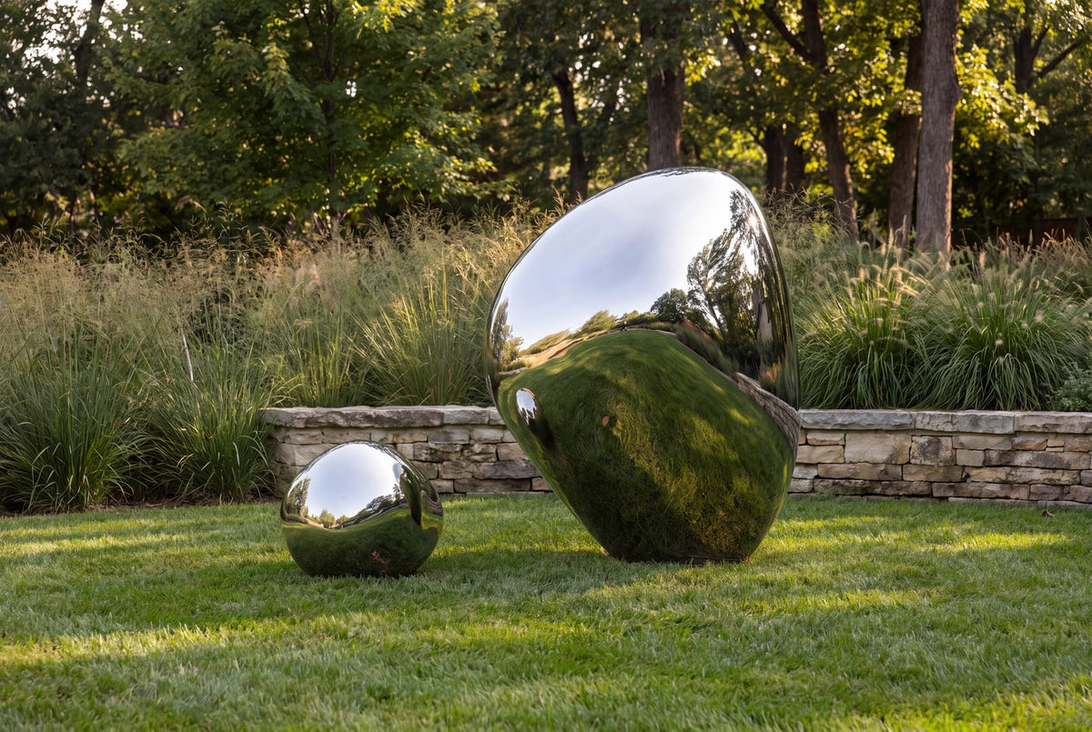 Two polished stainless steel stone forms among garden planting